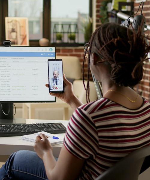 African american patient calling medic on telehealth videocall with webcam, using smartphone to attend online videoconference with physician. Talking about medicare on telemedicine call.